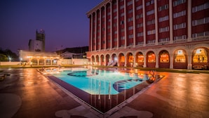 Un hotel con piscina, un edificio imponente con columnas y una torre al fondo.
