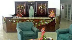 A reception area with a wooden desk, two green armchairs, and a floral arrangement on the desk. - The Downtown Hotel (Soufrière)