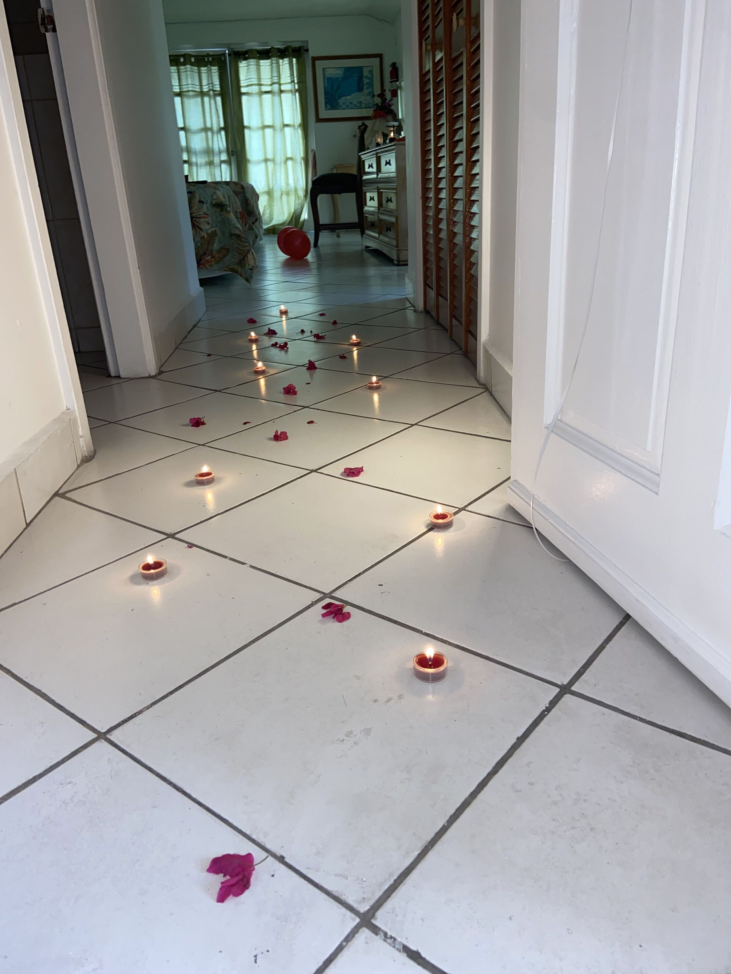 Un pasillo con piso de baldosas, varias velas encendidas y pétalos de rosa esparcidos.