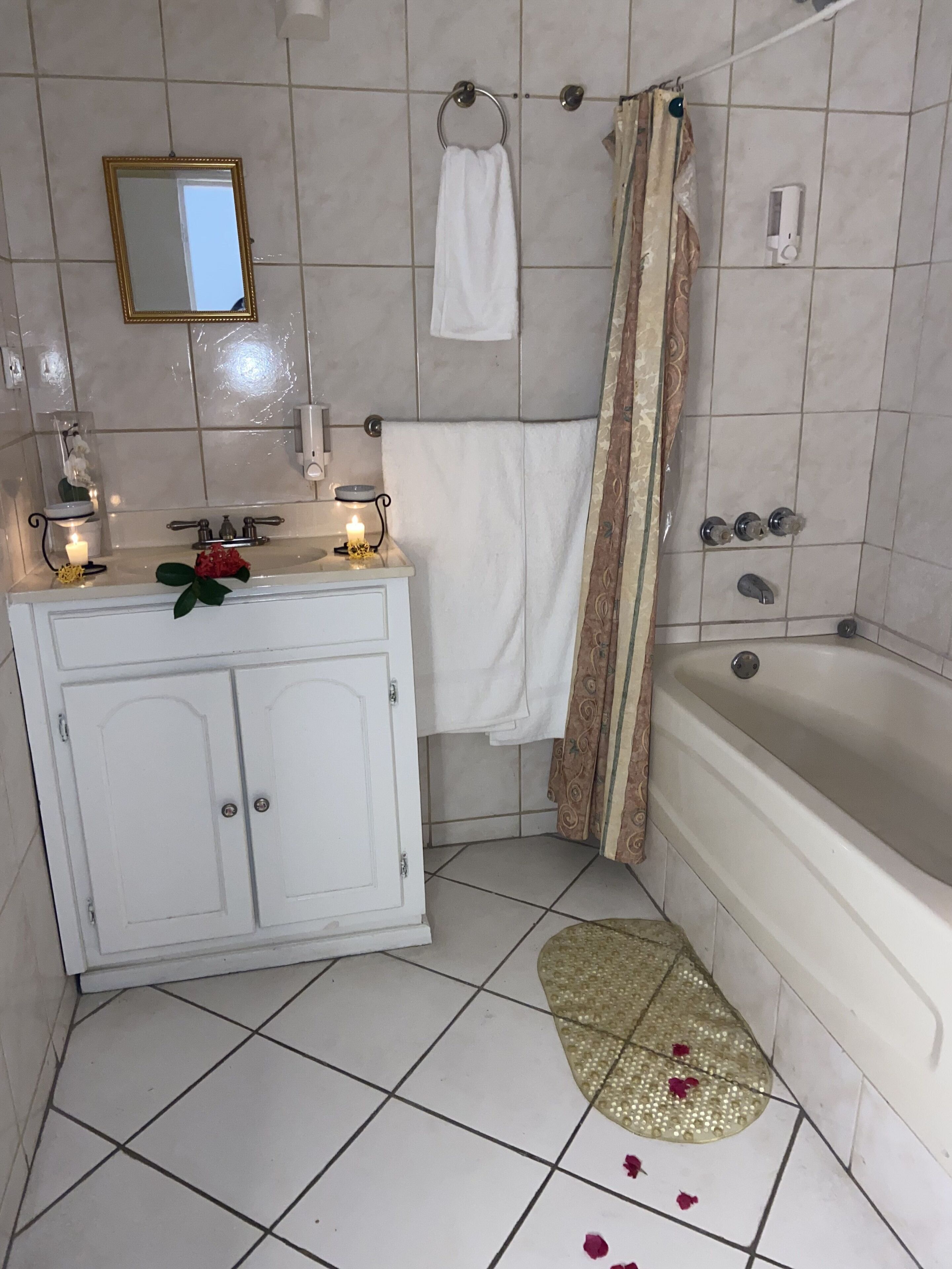 A bathroom with a bathtub, a vanity with a mirror, a towel rack, and a shower curtain.