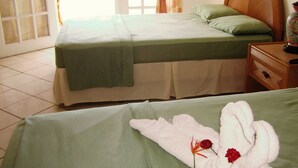 A hotel room with two beds, a wooden headboard, a nightstand with a lamp, and a window with curtains. - The Downtown Hotel (Soufrière)