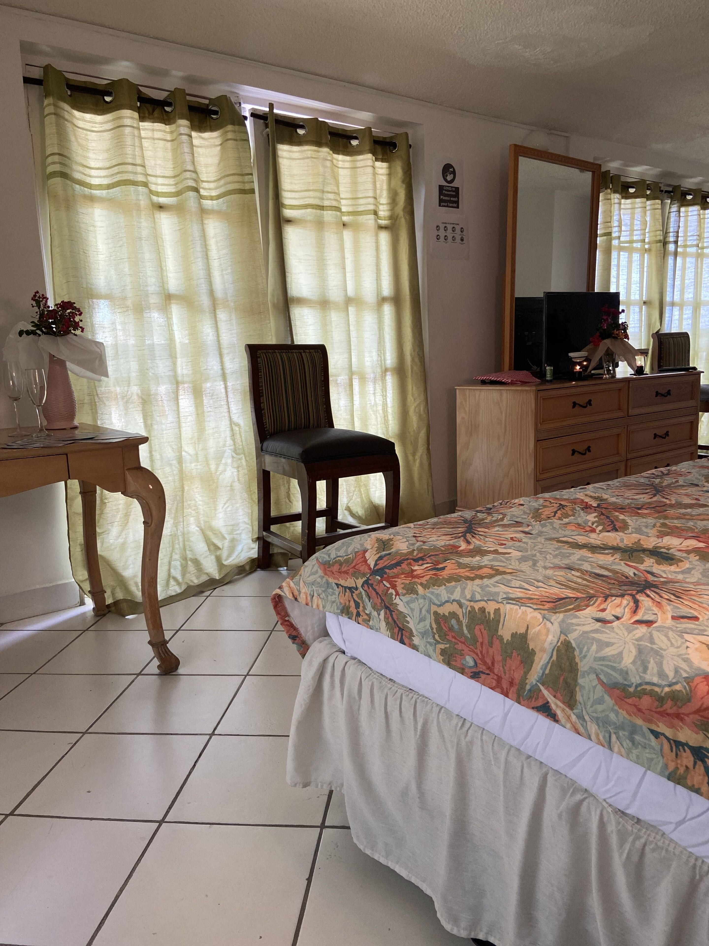 A bedroom with a bed, a chair, a desk, a dresser, a mirror, and curtains.
