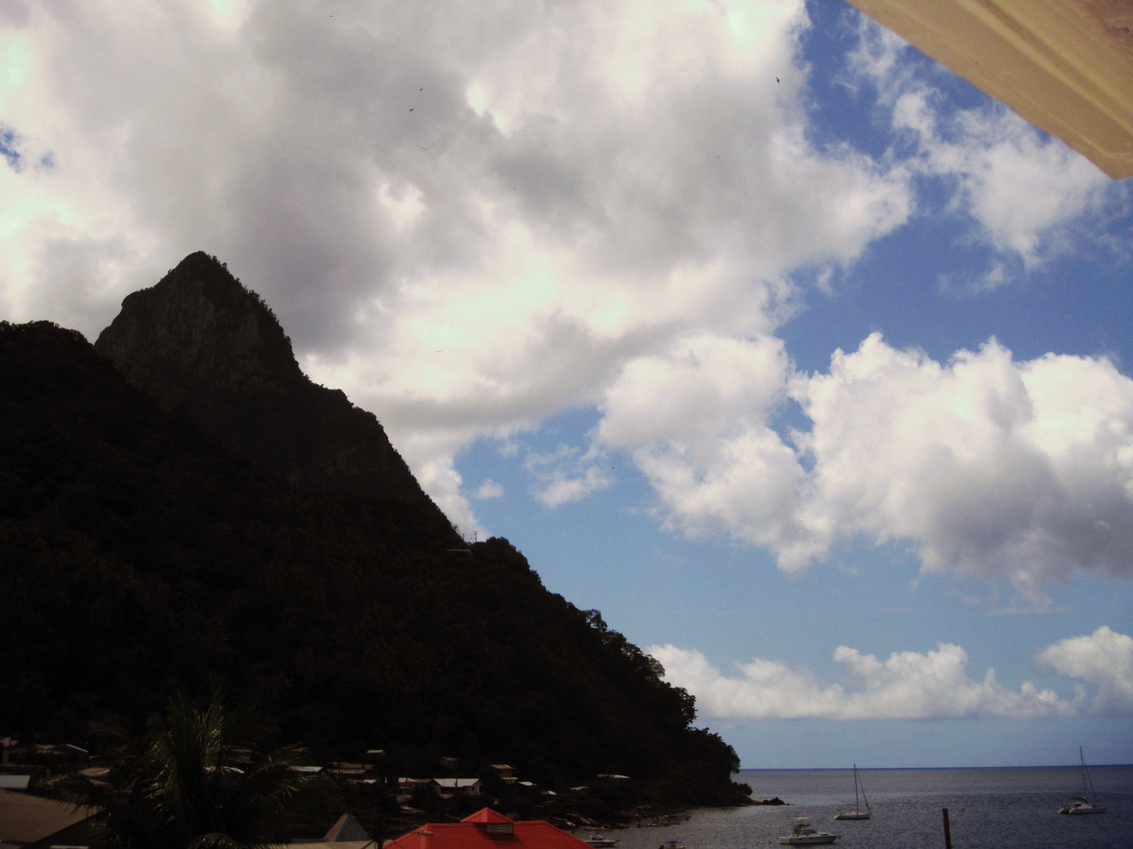 A coastal landscape with a prominent mountain, a clear sky, and several boats on the water.