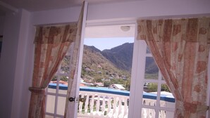 A room with a balcony, white walls, and a view of a mountainous landscape. - The Downtown Hotel (Soufrière)