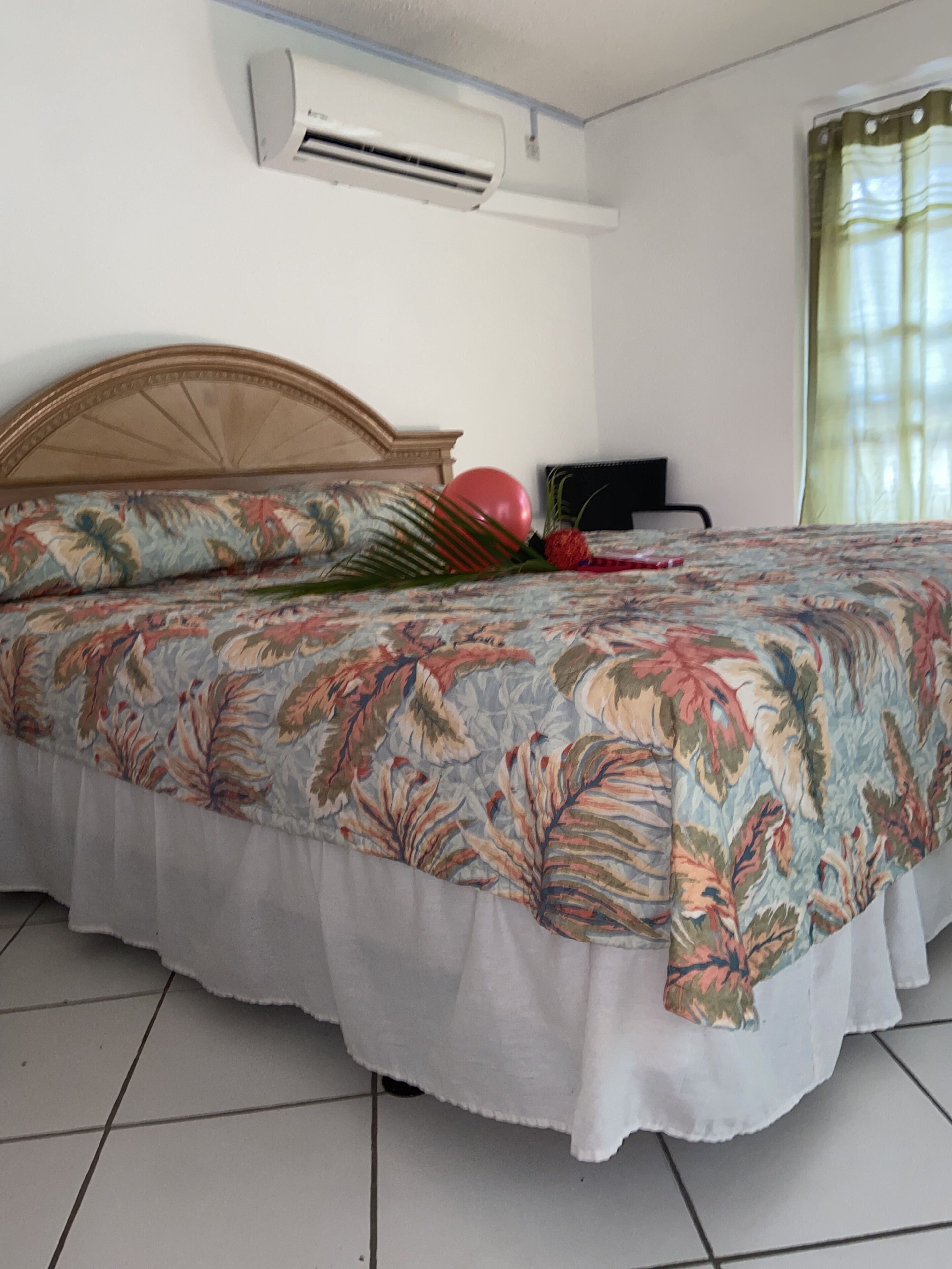 A bedroom with a bed, an air conditioner, a nightstand, and a window with curtains.