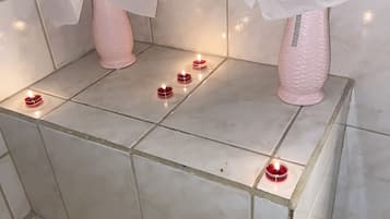 A bathroom with a tiled floor, a bathtub, and two pink vases with flowers on a pedestal.