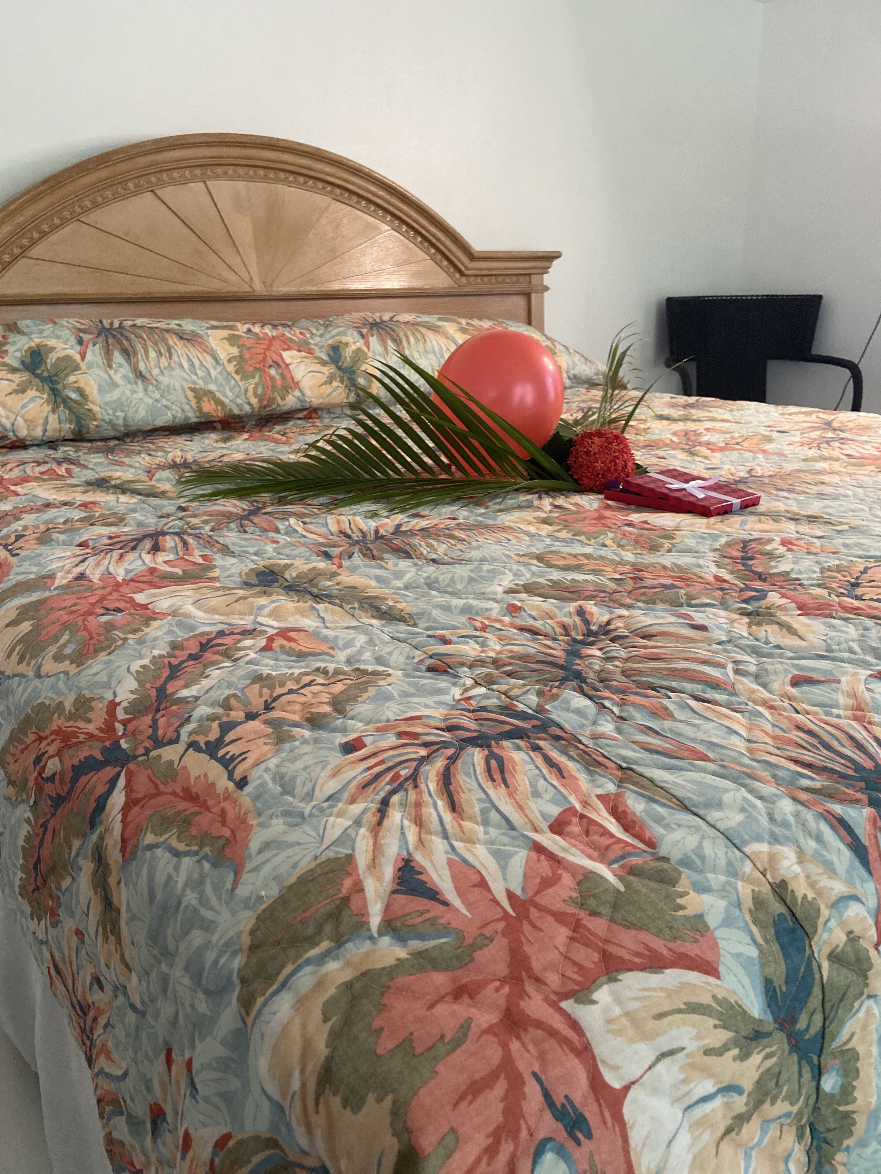 A bed with a floral bedspread, a red balloon, and a small gift box.