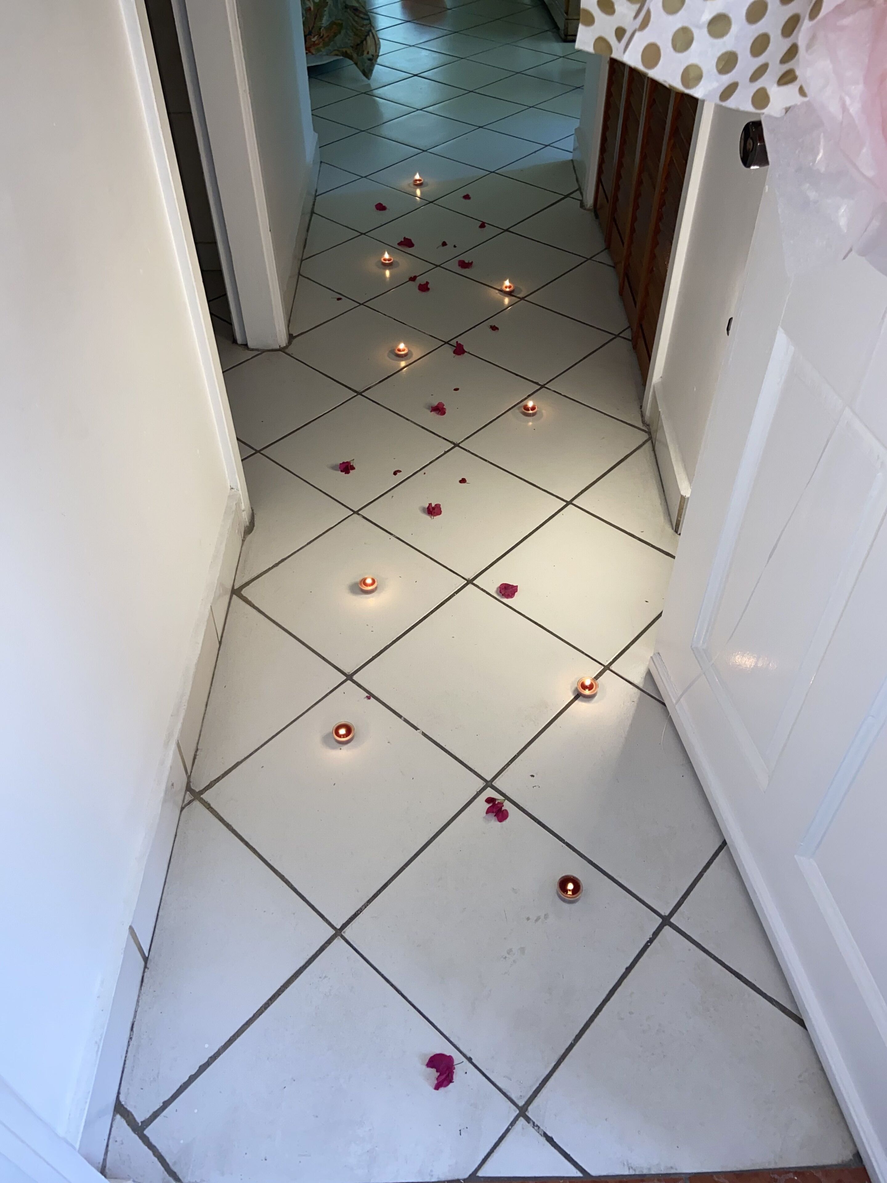 A hallway with white tiled flooring, small candles, and scattered rose petals.