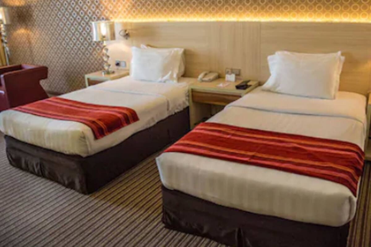 A hotel room with two beds, each with a red and white striped blanket, a bedside table with a lamp, and a telephone.