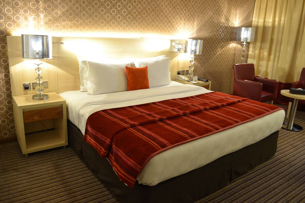 A hotel room with a large bed, two bedside tables, a nightstand, a red chair, and a small table.
