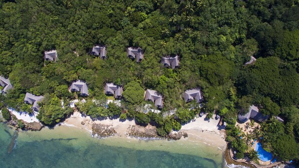 An aerial view of a coastal resort with multiple bungalow-style buildings surrounded by dense tropical vegetation and a sandy beach. - Fumba Beach Lodge (Fumba)