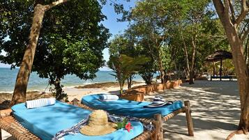 Relax in a tranquil beach setting with two hammocks under the shade of large trees, offering a scenic ocean view.