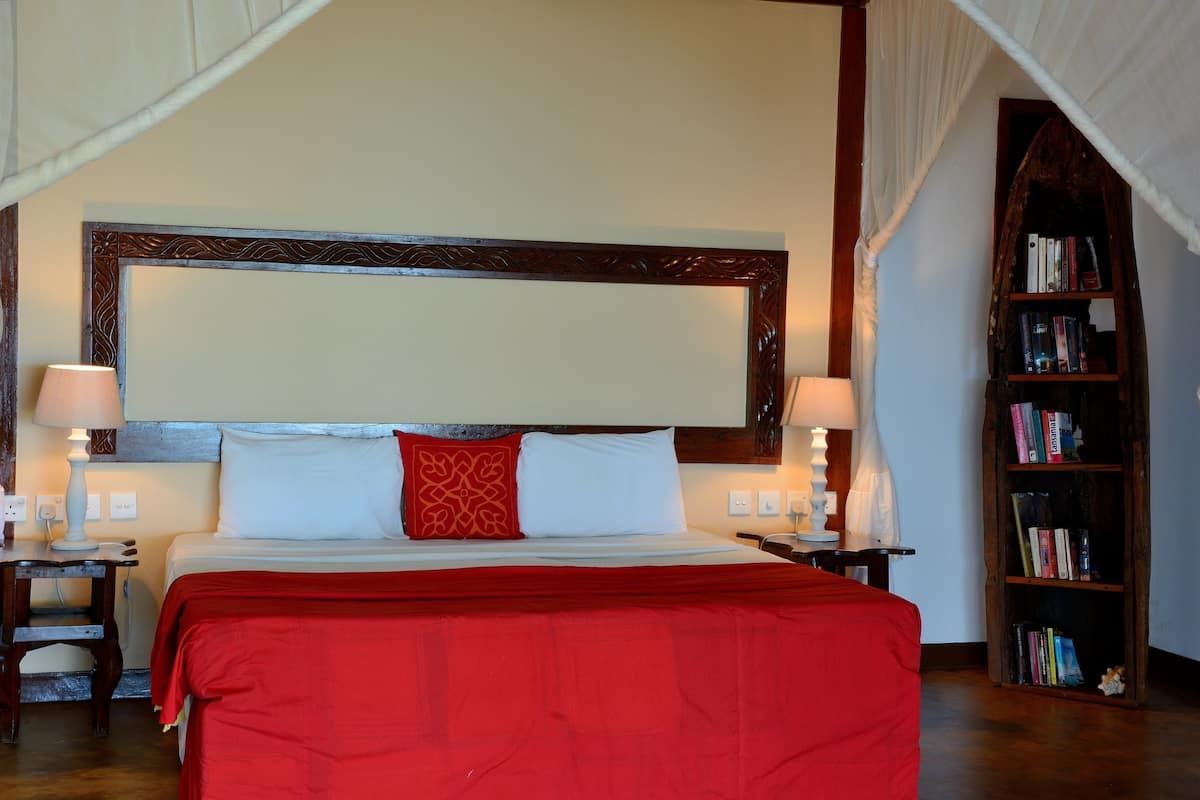 A hotel room with a large bed, two bedside tables with lamps, a bookshelf, and a canopy bed.