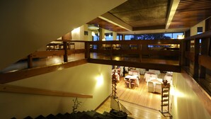 A spacious interior with a wooden staircase leading to a lower level, a dining area with tables and chairs, and a view of the outdoors through large windows. - Hotel de Castro (Castro)