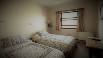 Una habitación con dos camas, una ventana con cortinas, una mesita de noche y un radiador.