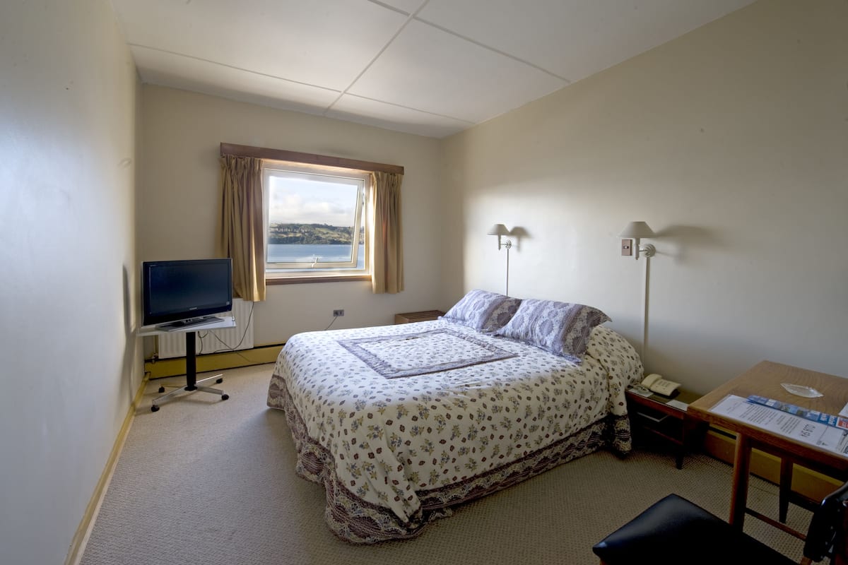 A bedroom with a bed, a desk, a television, and a window with curtains.
