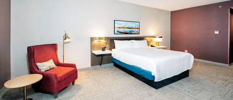Ein Hotelzimmer mit einem Bett, einem roten Sessel, einem runden Tisch und zwei Nachttischlampen.