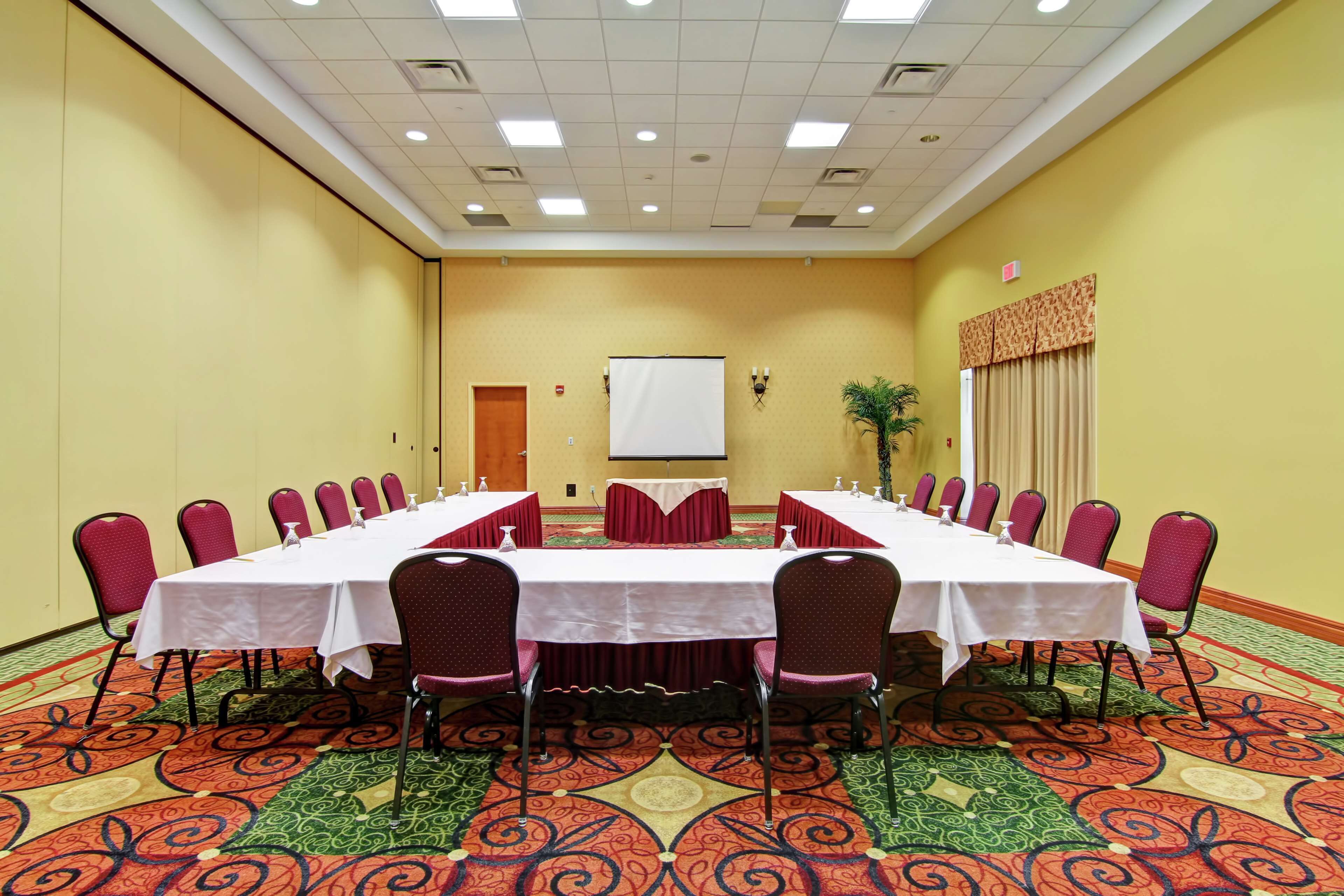 A conference room with a long table, red chairs, and a projector screen.