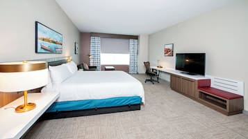 A hotel room with a bed, desk, TV, and a window with curtains.