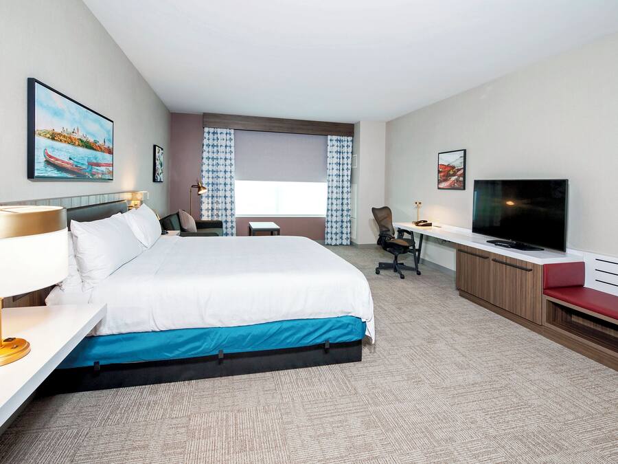 A hotel room with a bed, desk, TV, and a window with curtains.