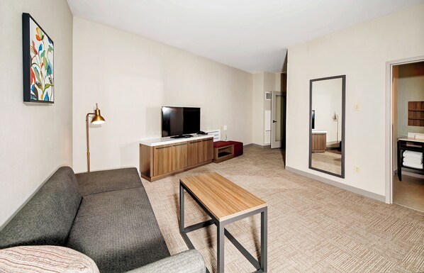 Un salon moderne avec un canapé, une table basse en bois, un téléviseur et un miroir.