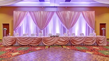 A banquet hall with a long table set for a formal event, draped curtains, and a patterned carpet.