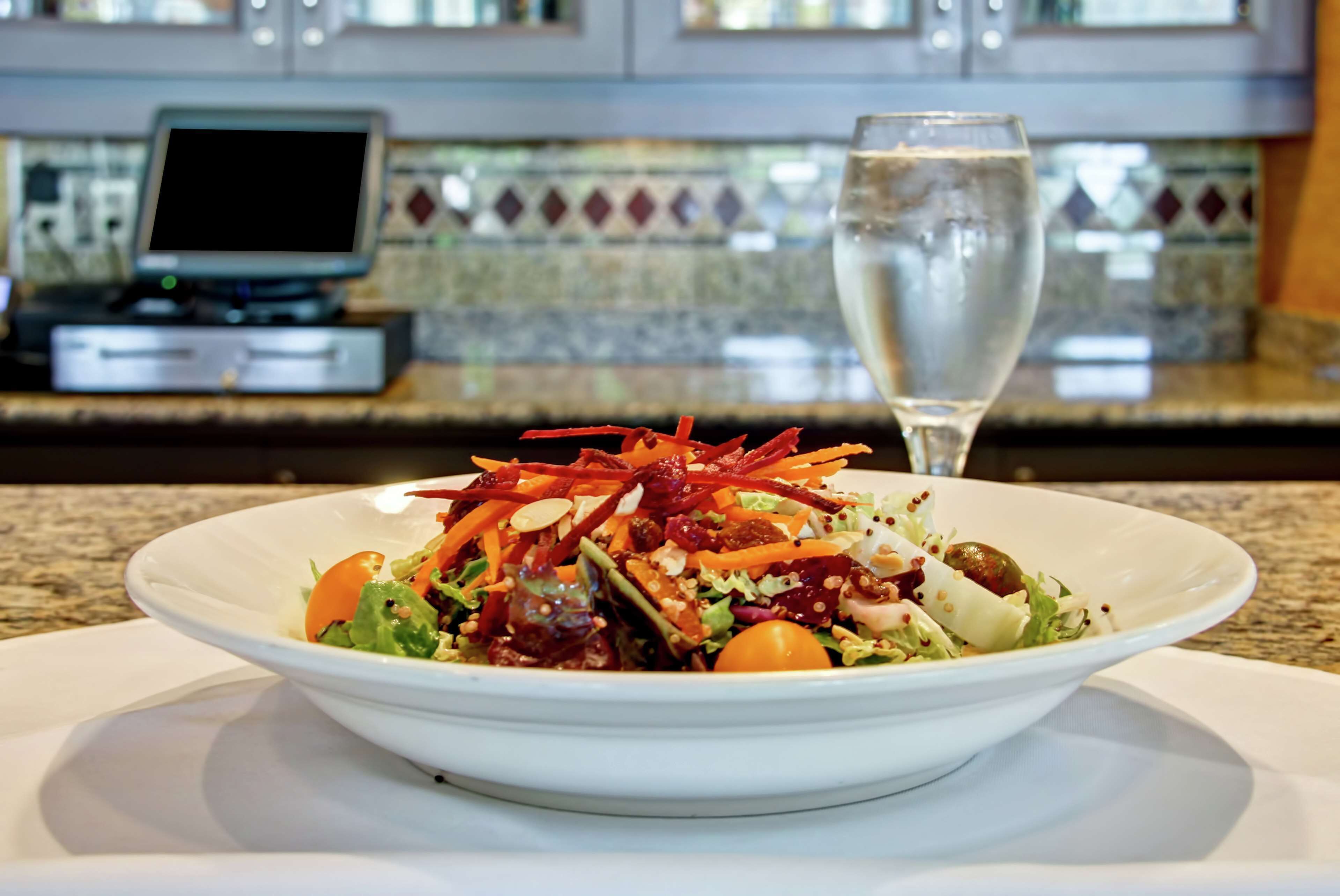 A white bowl of salad with a glass of water on a table in a restaurant.