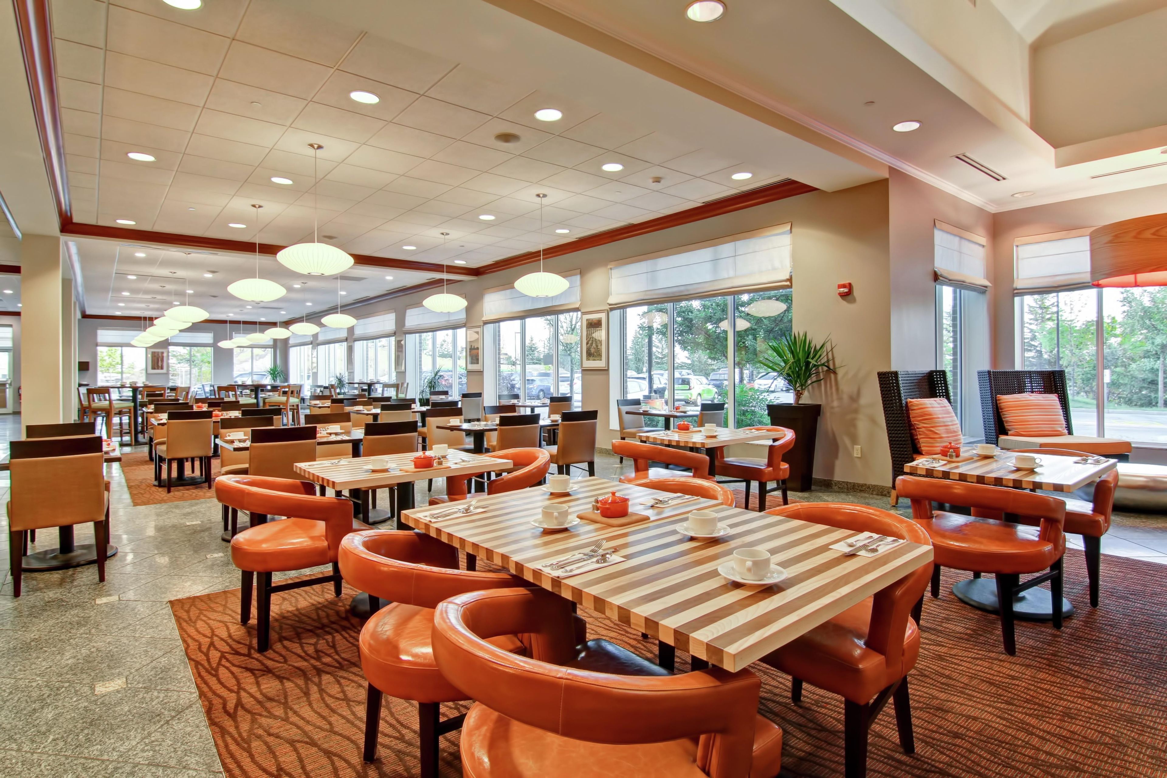 A spacious dining area with multiple tables and chairs, large windows, and ceiling lights.