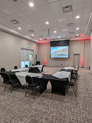 Ein Konferenzraum mit Tischen, Stühlen, einer Projektionsleinwand und Teppichboden.