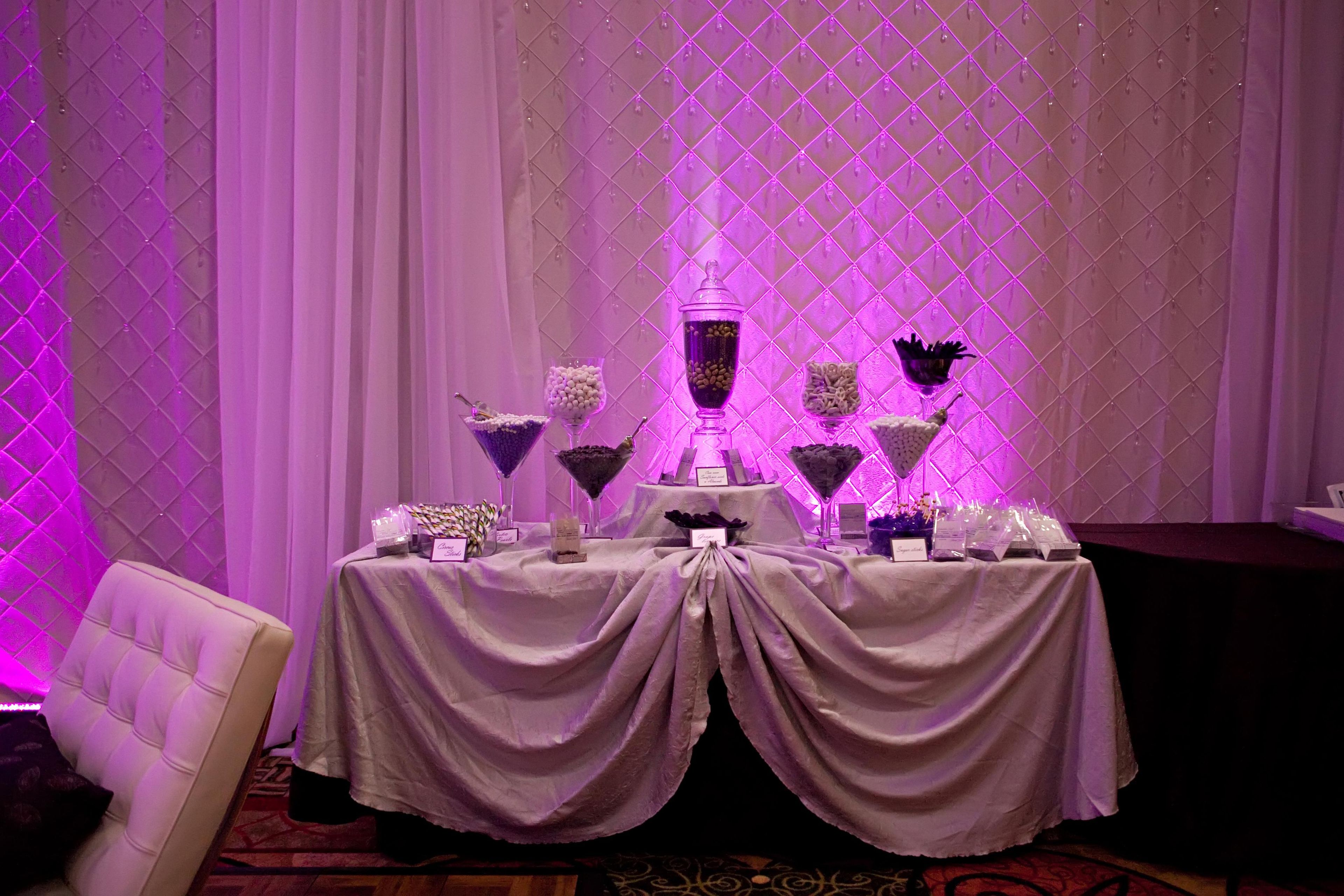 A table set up with various food items and a decorative centerpiece against a backdrop of curtains and a diamond-patterned wall.