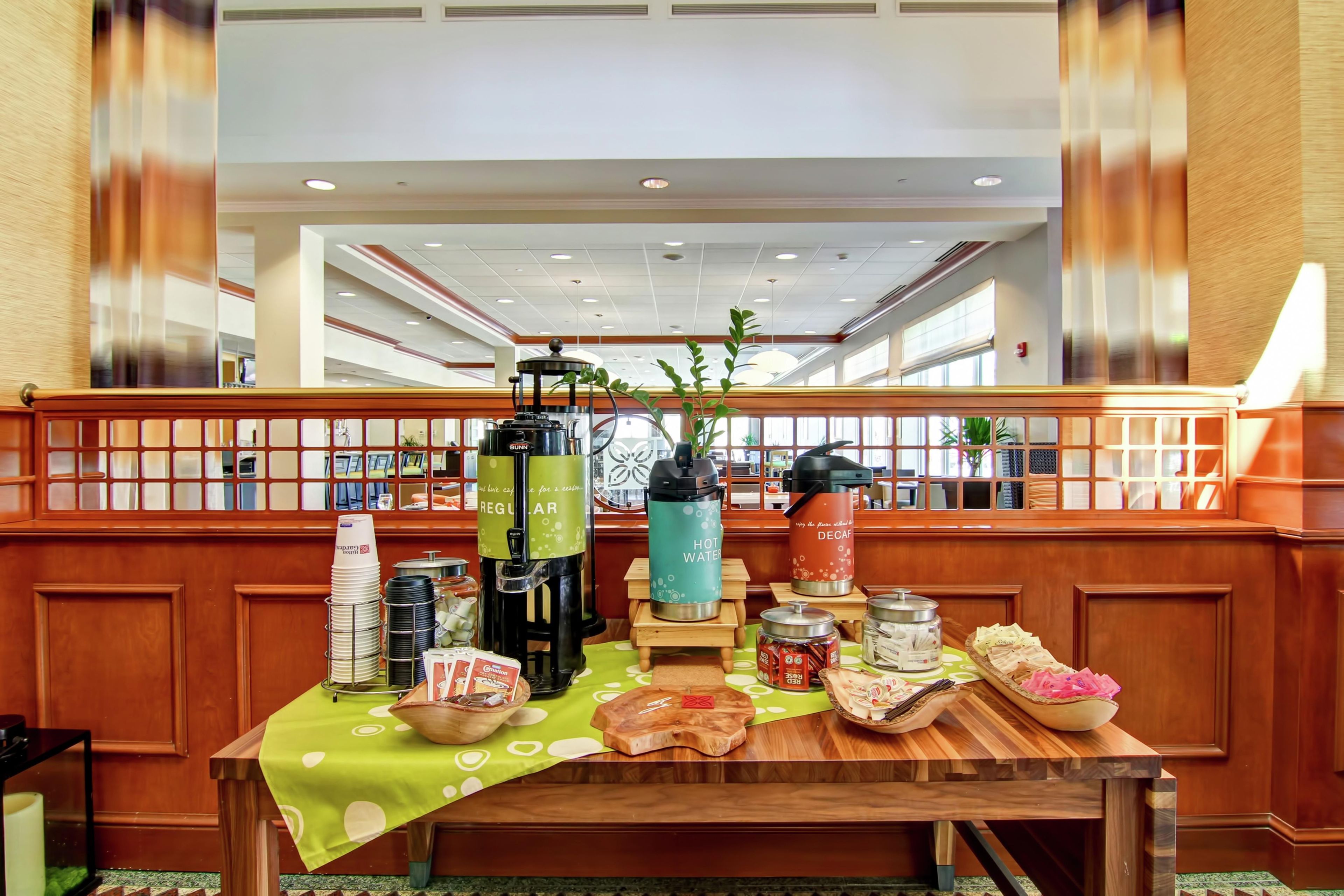 A hotel lobby with a reception desk, a coffee station, and a seating area.