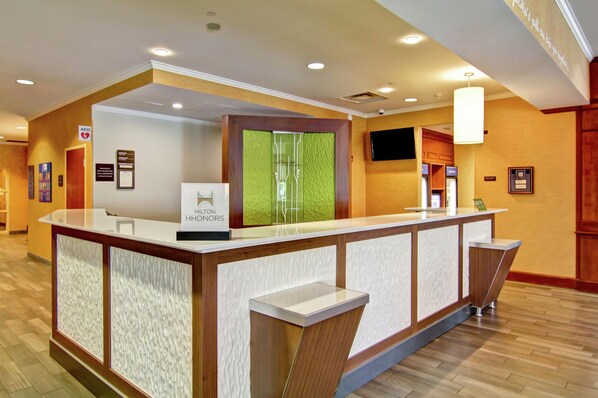Una recepción de hotel con un cartel de Hilton Honors, una pared texturizada de color verde y un televisor de pantalla plana montado en la pared.