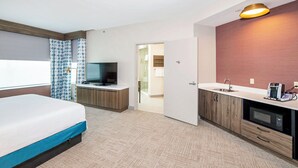 Une chambre d’hôtel équipée d’un lit, d’une télévision, d’une kitchenette et d’une salle de bain visible à travers une porte ouverte.