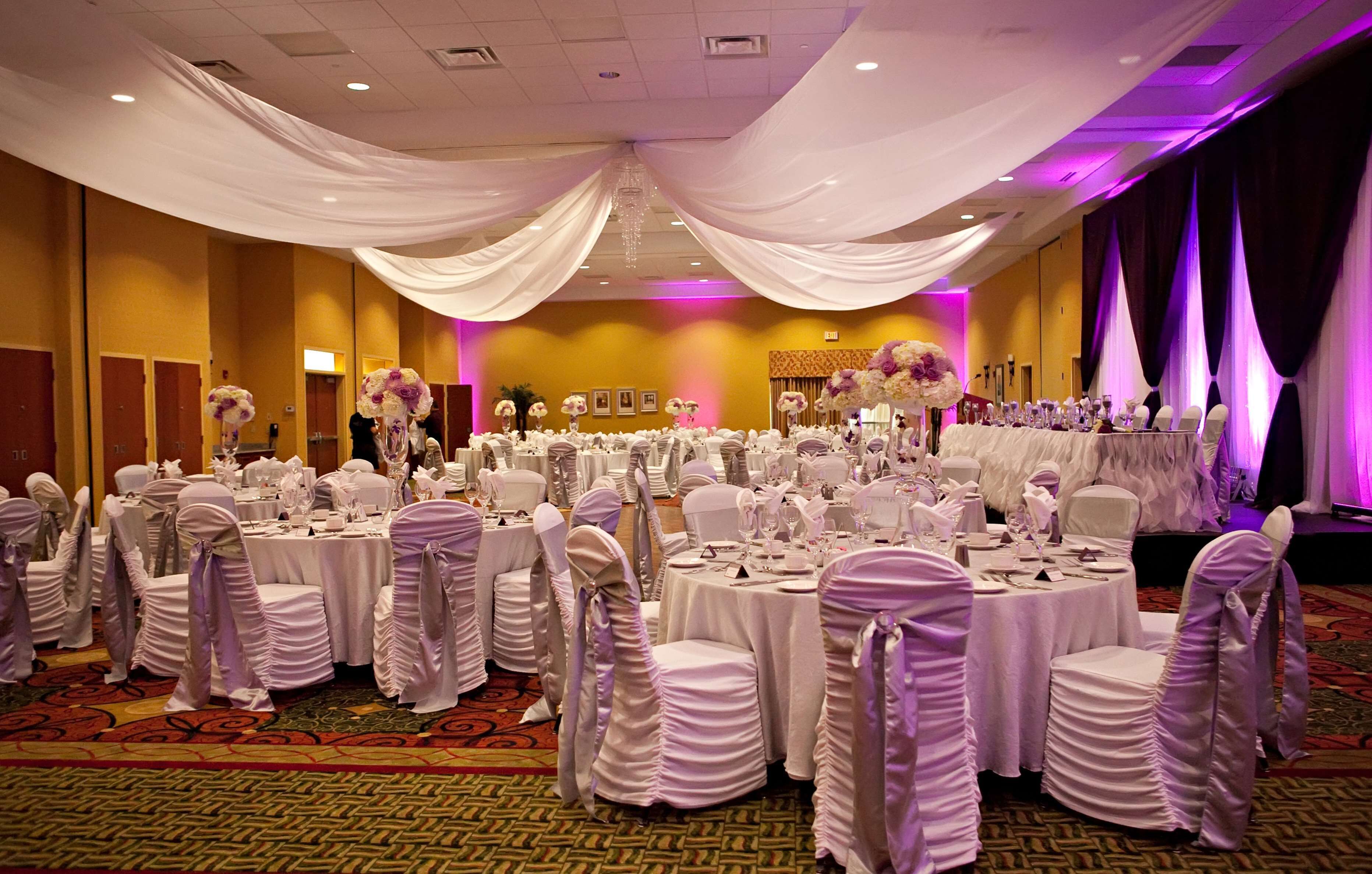 Un salón de banquetes con mesas redondas cubiertas con manteles blancos, sillas con fundas blancas y centros de mesa florales.