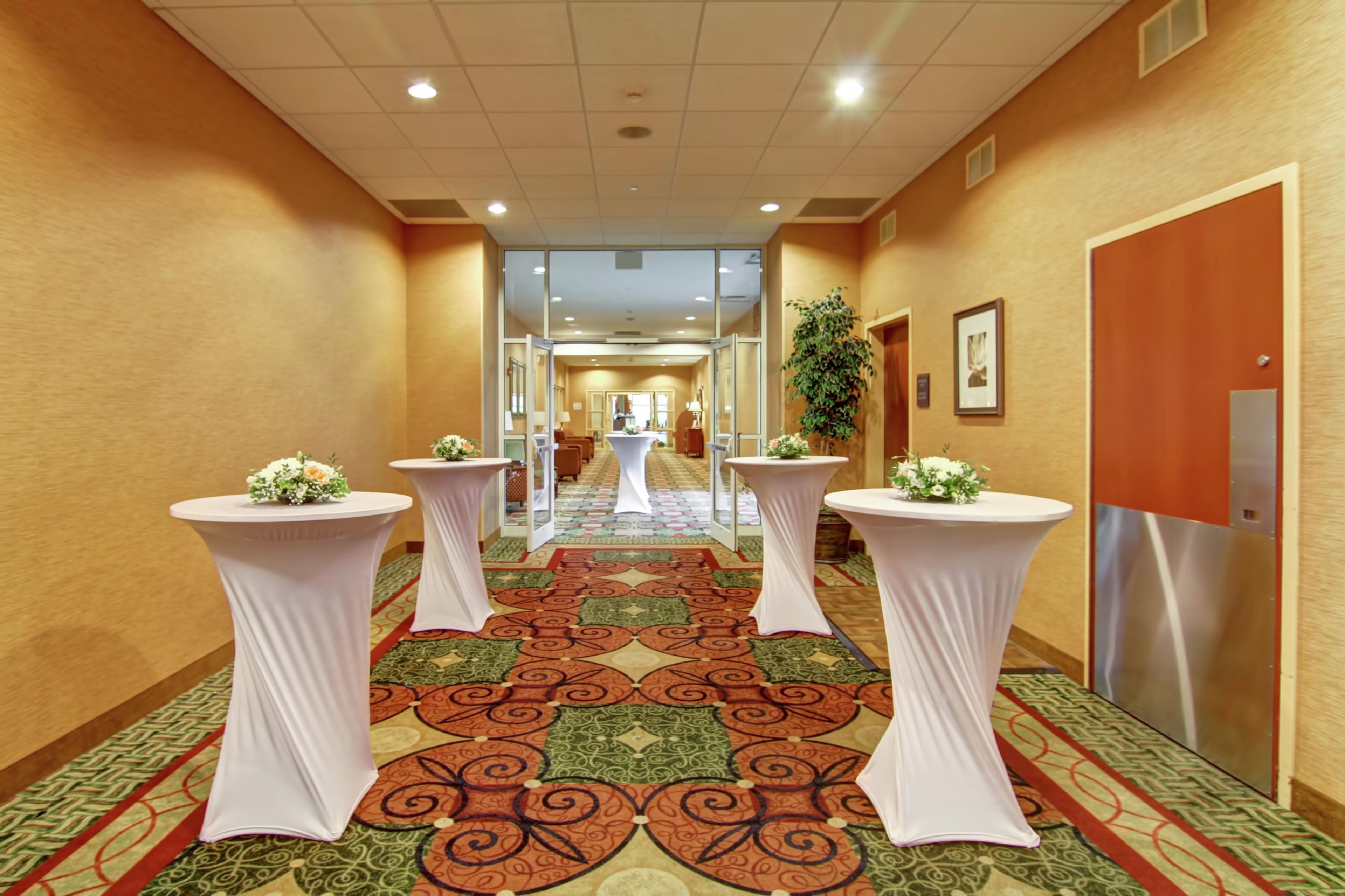 A hotel corridor with a patterned carpet, white columns with floral centerpieces, and a door on the right.