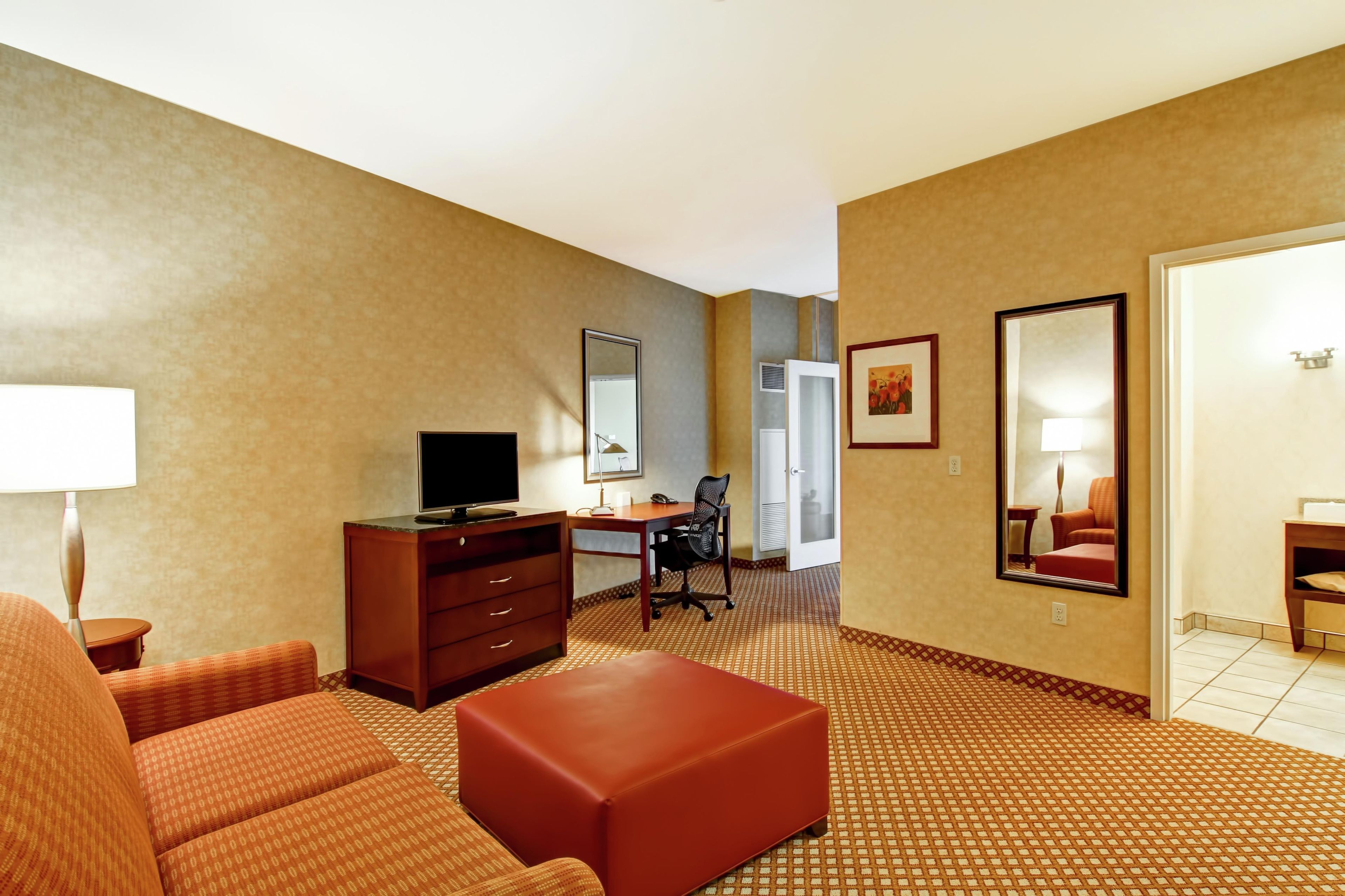 Habitación de hotel con sofá, televisión, escritorio, silla, espejo y alfombra estampada.