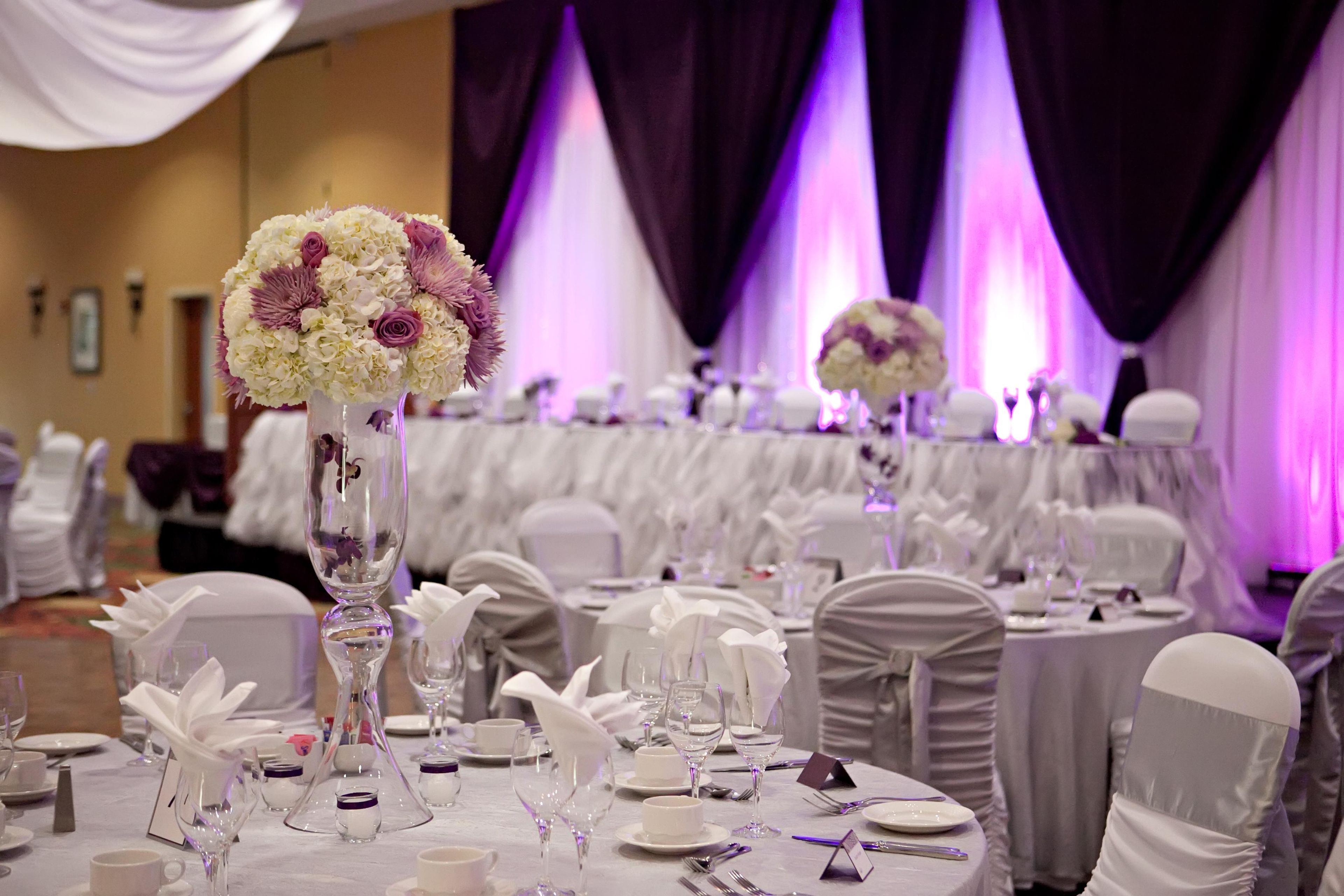 Un salón de banquetes con mesas redondas dispuestas para un evento formal, con manteles blancos y centros de mesa florales.