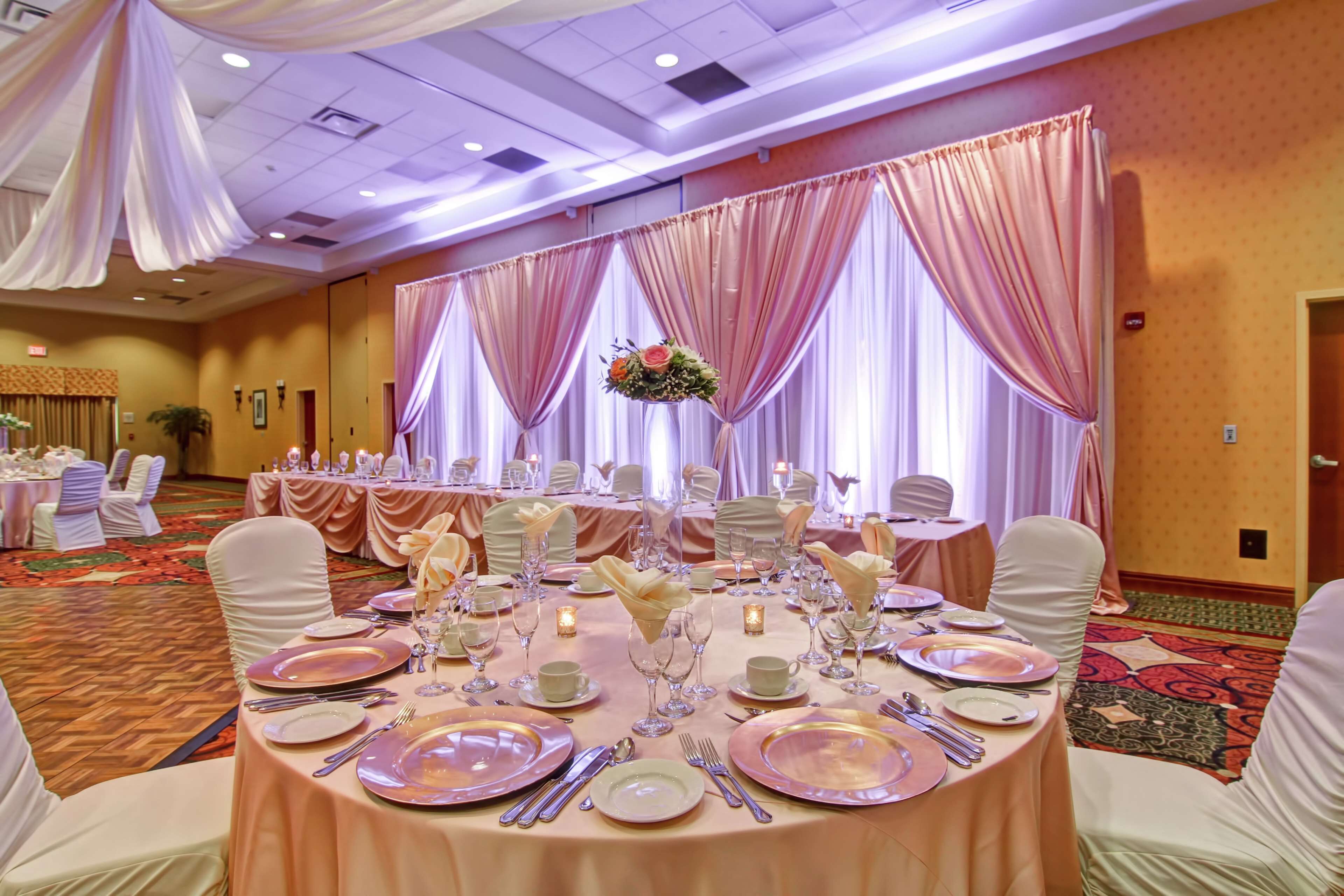 A banquet hall with round tables set for a formal event, featuring white and gold linens, and floral centerpieces.
