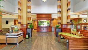 Un hall d’entrée spacieux avec un comptoir d’accueil en bois, des coins salon et des plantes en pot.