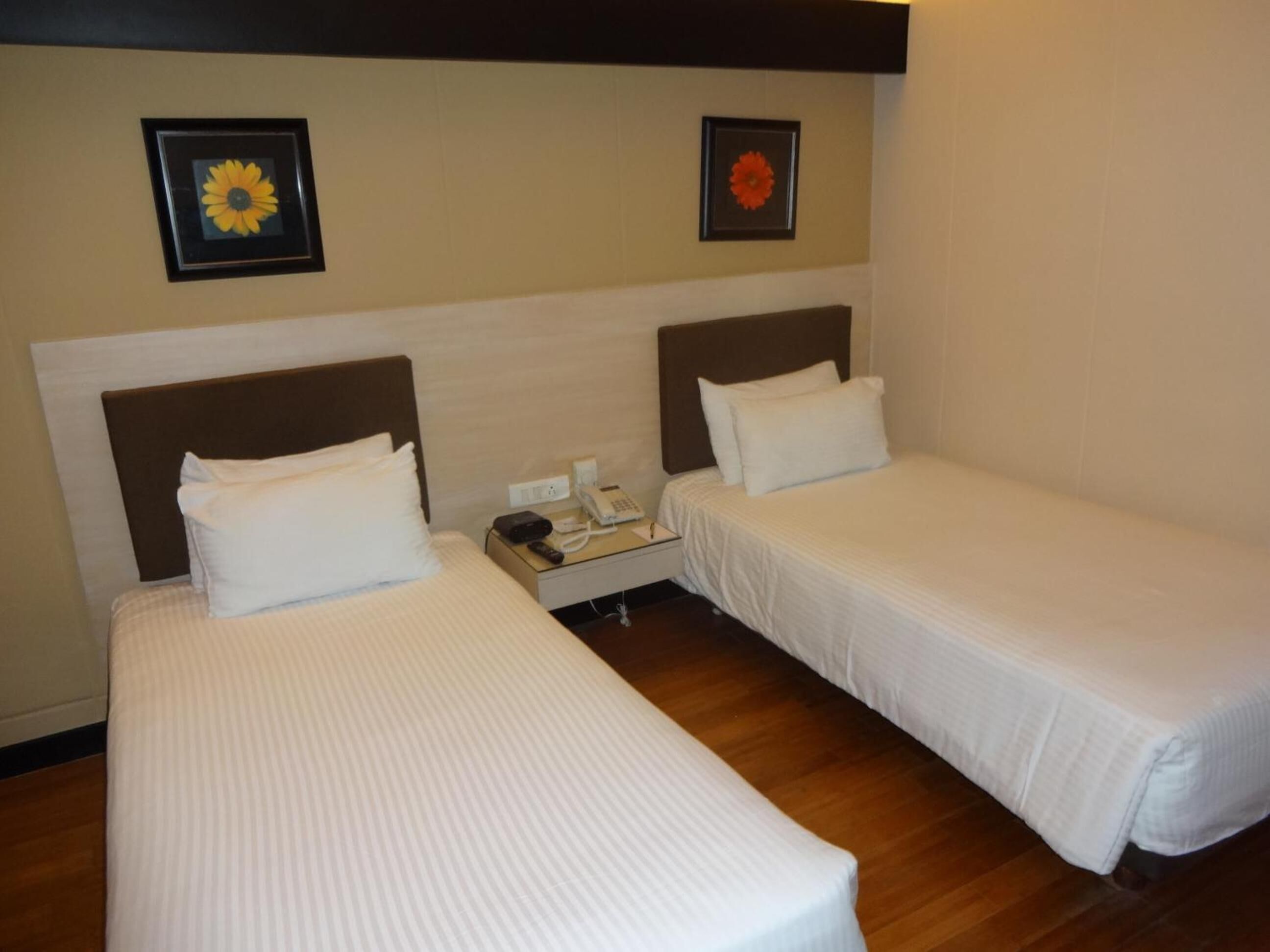 A hotel room with two single beds, a bedside table with a phone, and two framed pictures on the wall.