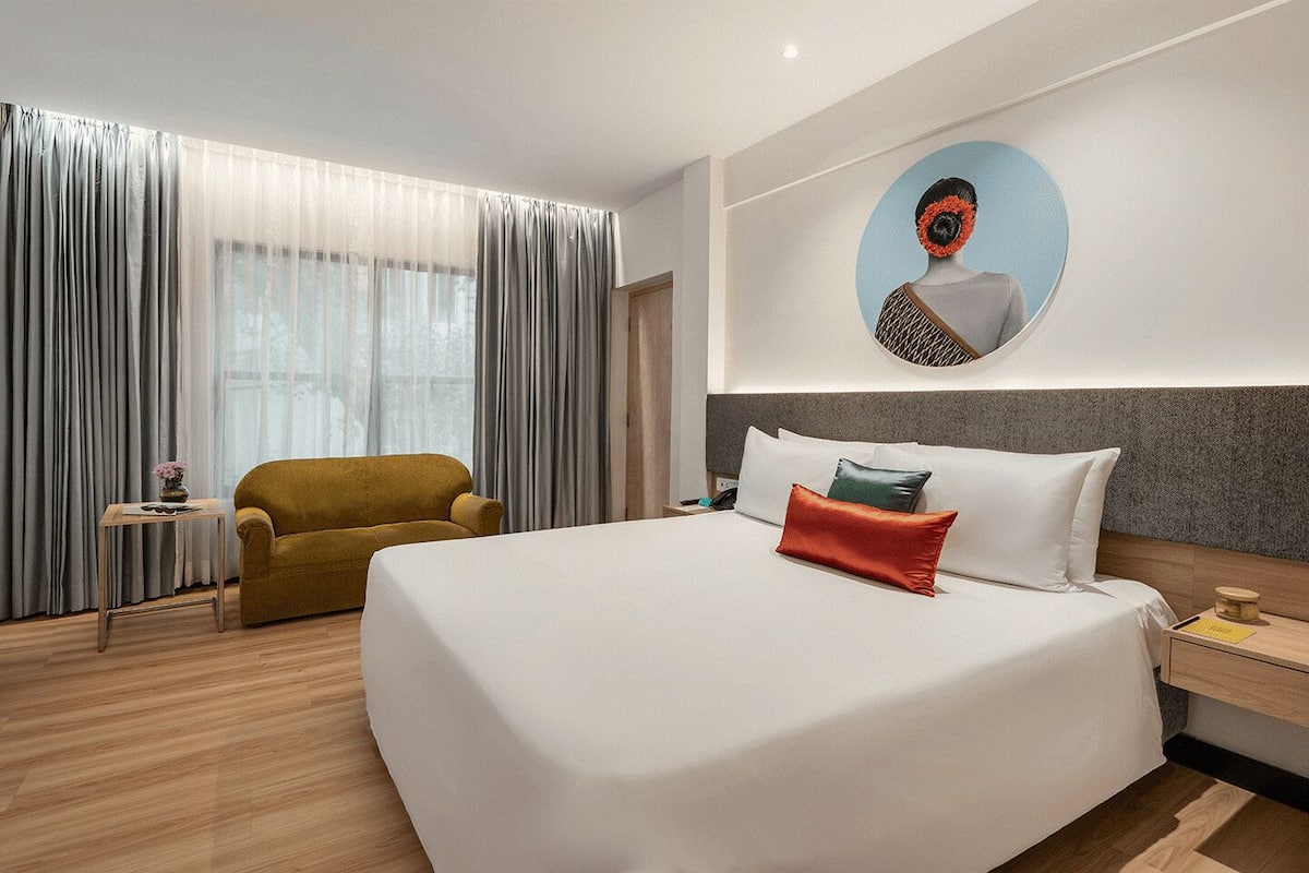 A hotel room with a large bed, a sofa, a small table, and a wall-mounted artwork.
