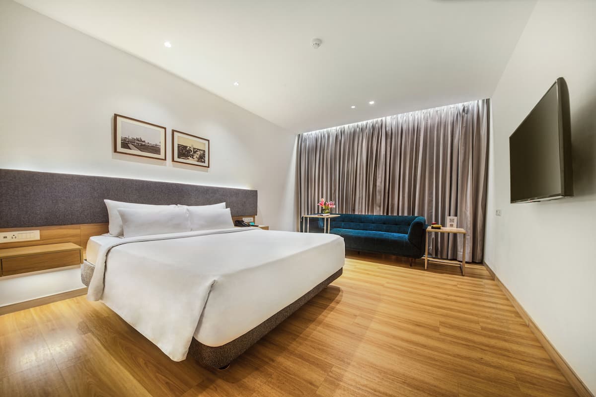 A modern hotel room with a large bed, a flat-screen TV, a desk, and a sofa.