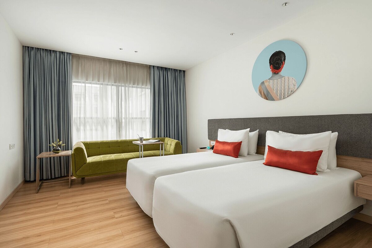 Una habitación de hotel con dos camas, un sofá verde, una mesita y un ventanal con cortinas.