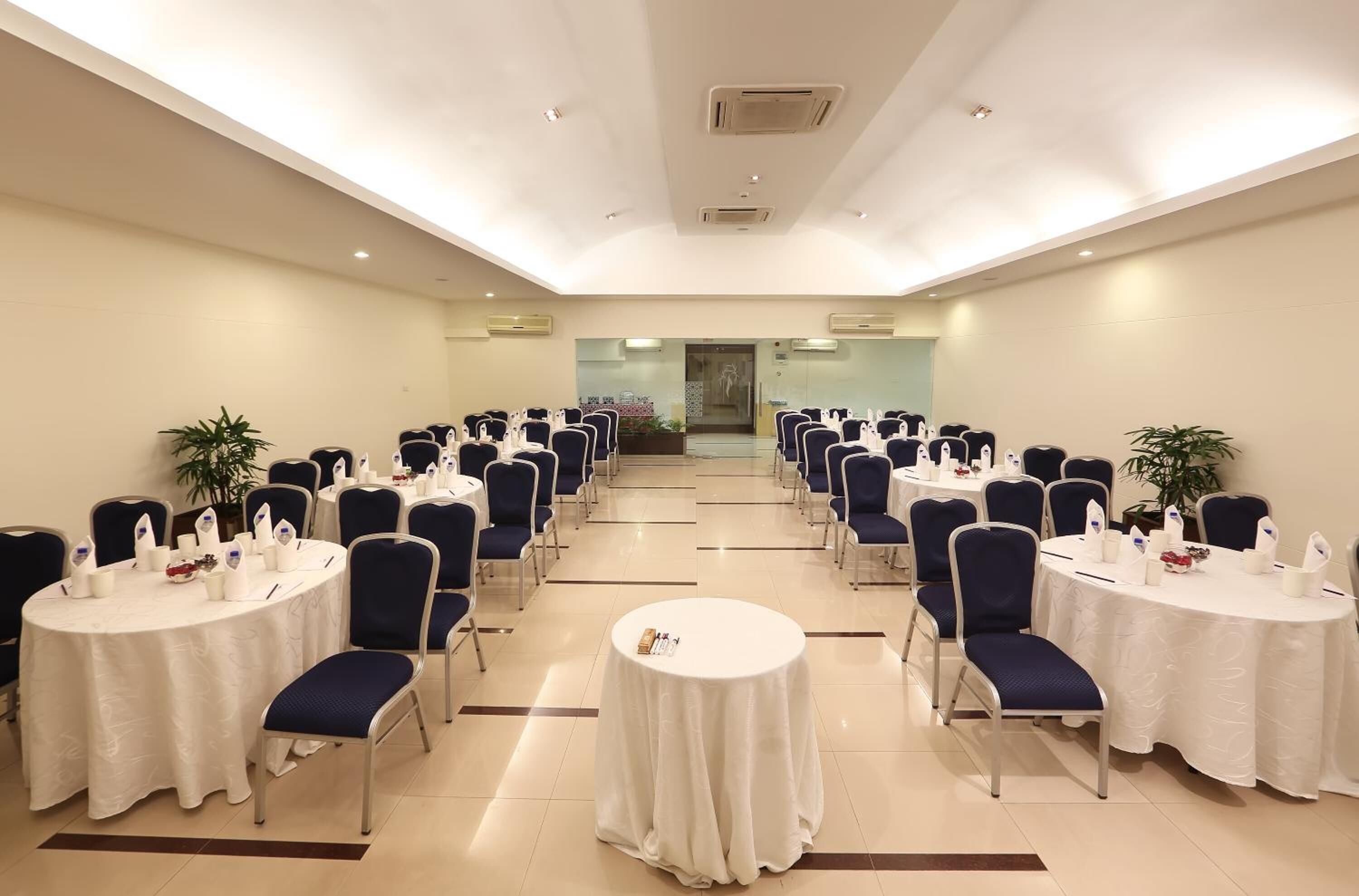Un salón de conferencias con varias mesas redondas, sillas azules y manteles blancos.