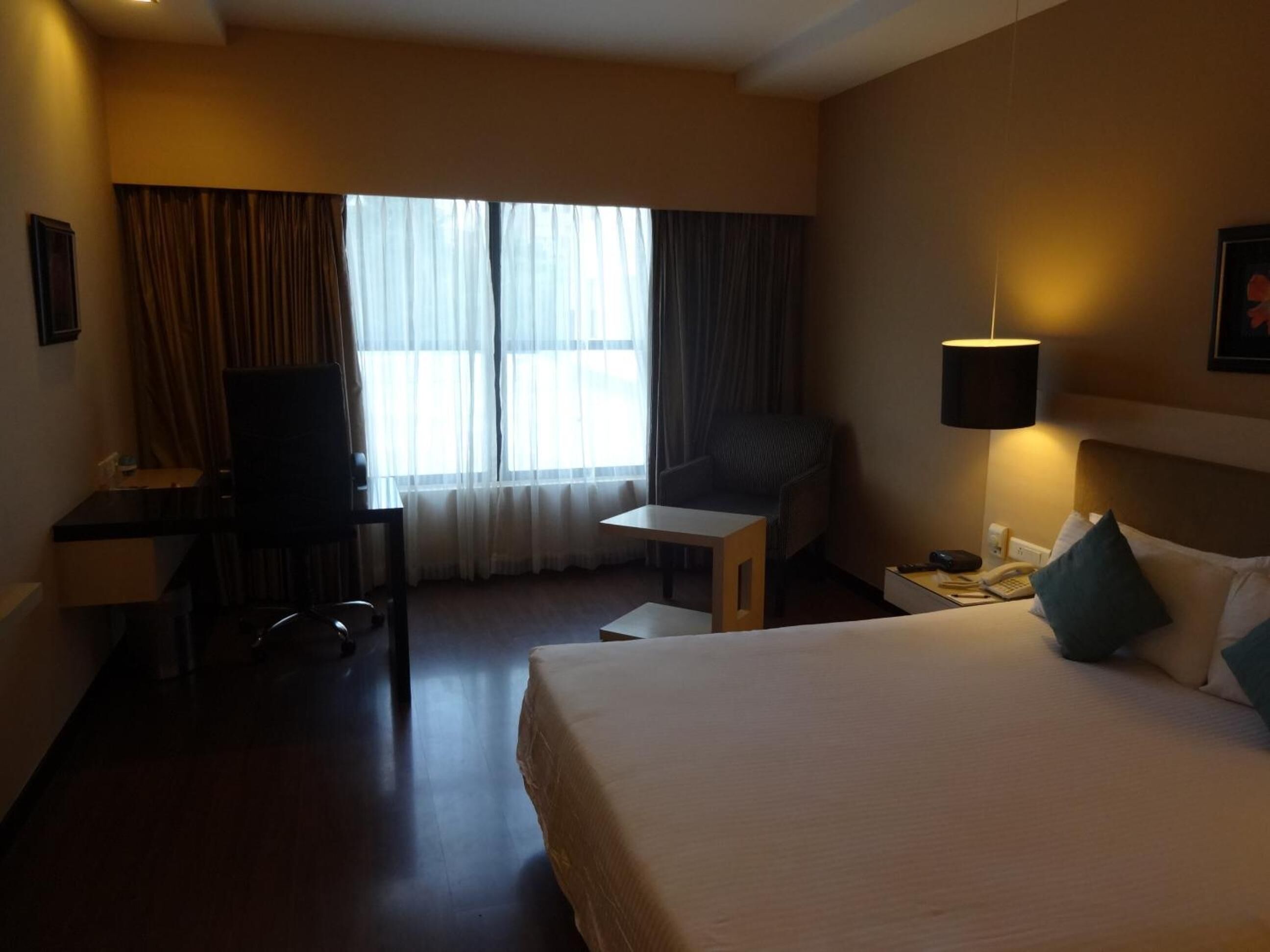 A hotel room with a bed, a desk, a chair, a TV, a lamp, and a window with curtains.