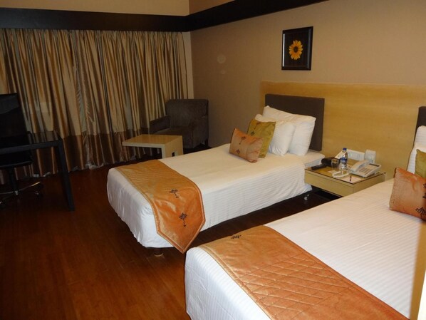 Habitación de hotel con dos camas, un escritorio, una silla, un televisor y una decoración de girasol en la pared.