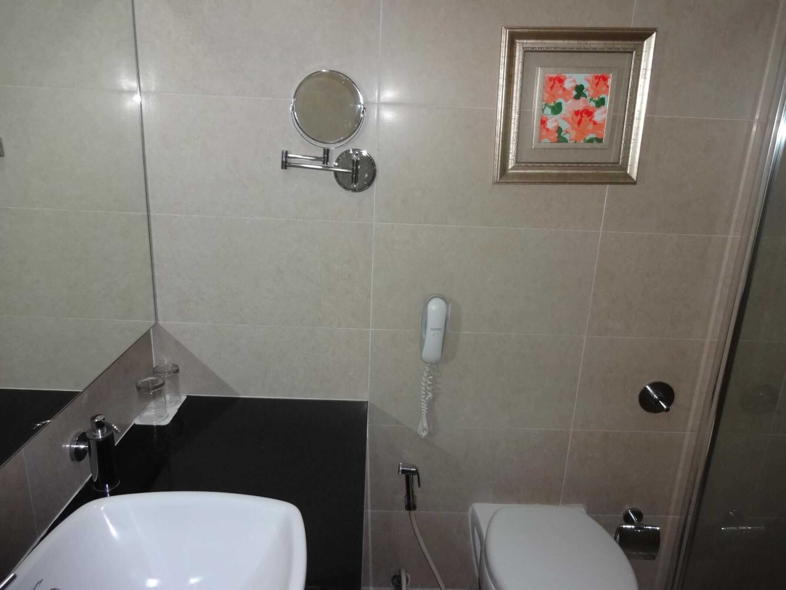 A bathroom with a white sink, a toilet, a mirror, and a telephone.