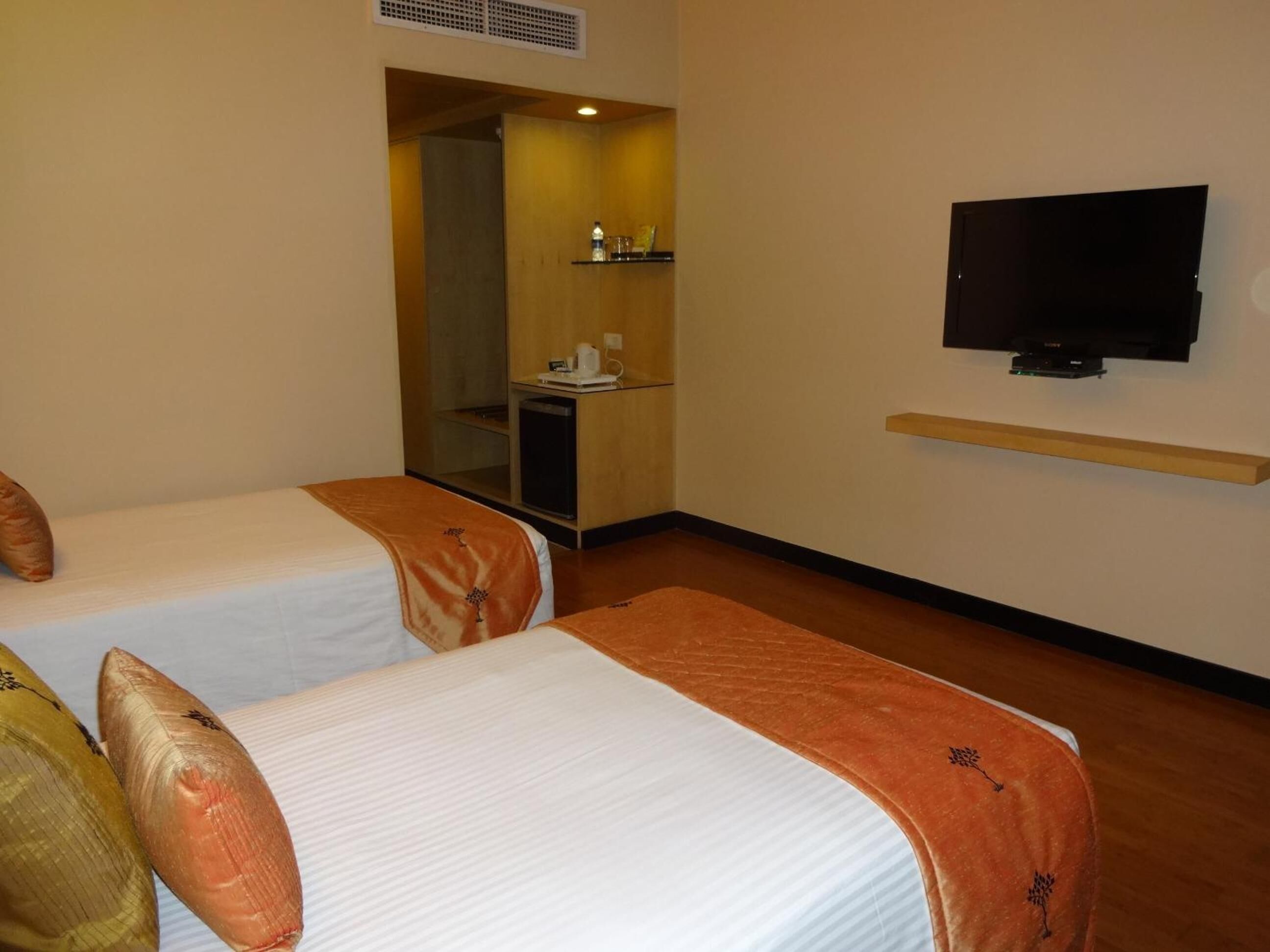 A hotel room with two beds, a TV, a small desk, and a mirror.
