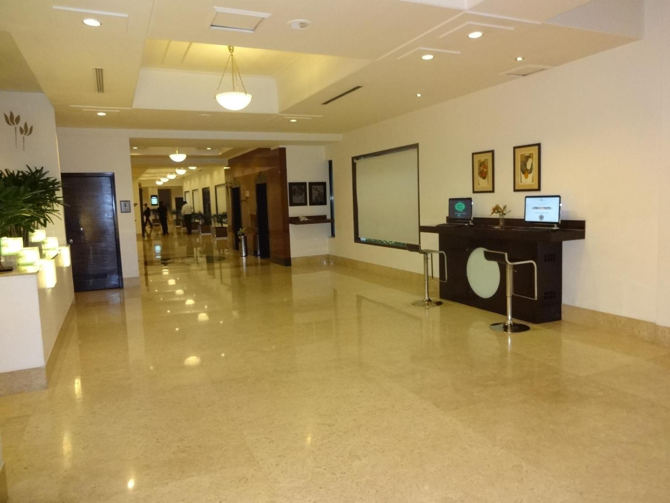 Zona de recepción de hotel con piso pulido, mostrador de recepción y una pantalla grande.