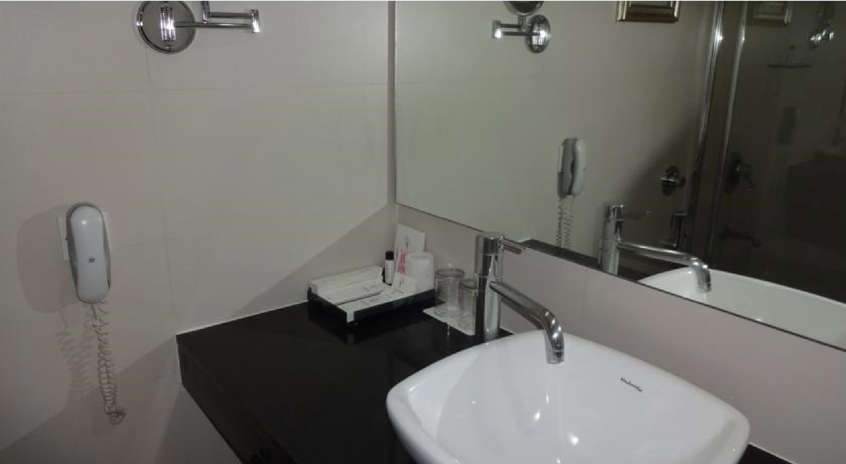 A bathroom with a white sink, a mirror, a telephone, and a black countertop.